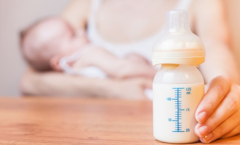A mother holds her baby and a bottle of breastmilk